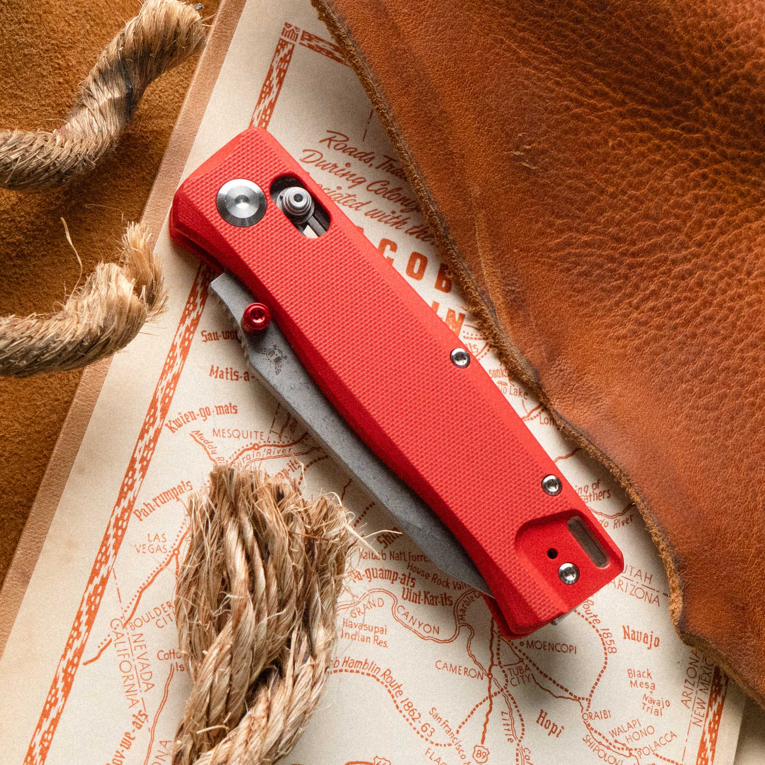 Flytanium BEEF folding knife in Fire Red, closed, resting on a vintage map and leather