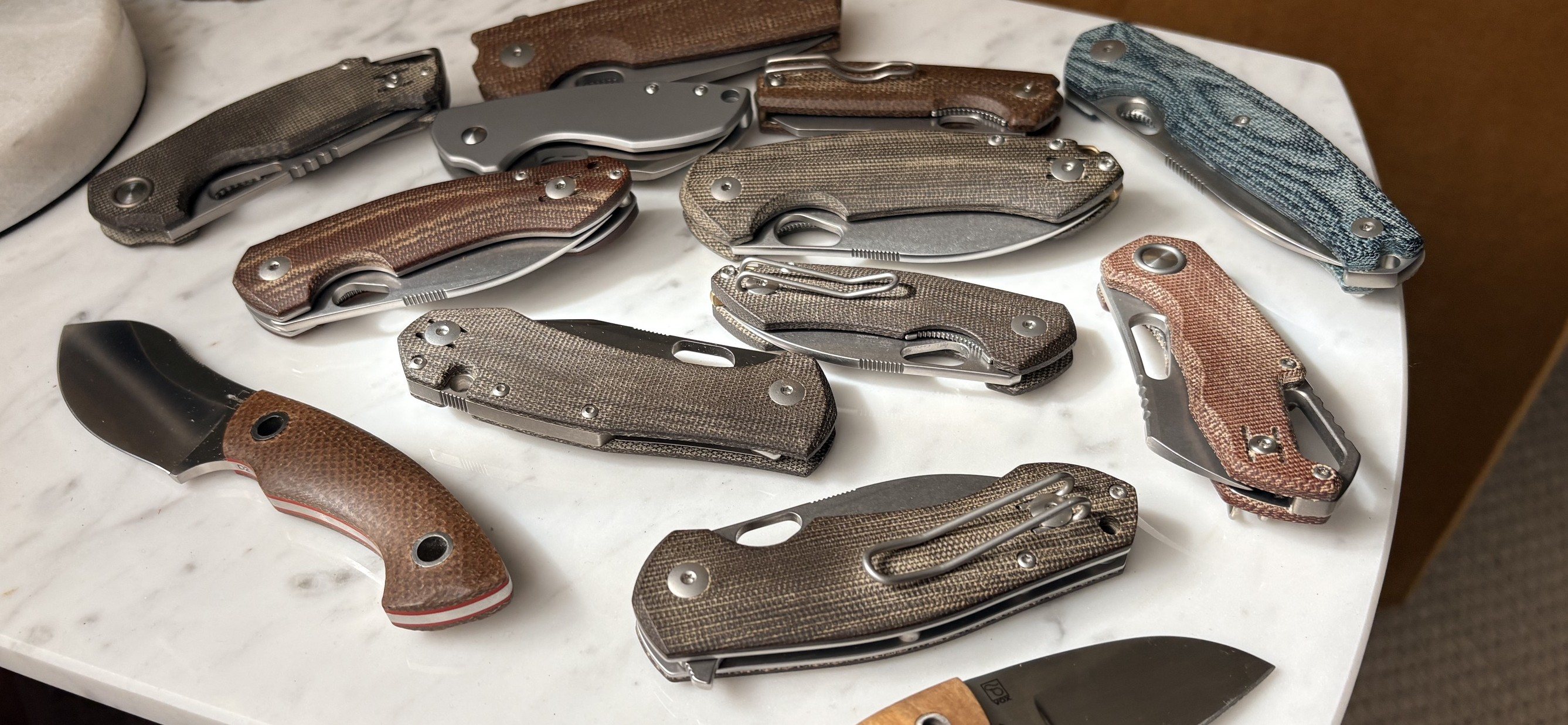 A year's rotation of EDC knives spread on marble